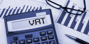 Electronic VAT calculator on desk with paperwork displaying financial graphs.