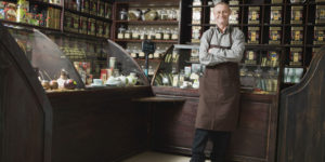 Image of a shop owner standing in an old-fashioned general store, illustrating the notion of deciding to sell your limited company