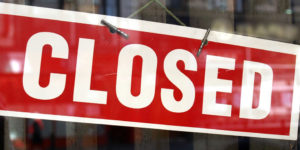 A rectangular 'closed' sign with white lettering on a red background, hanging in a shop window, used to represent the process of dissolving a limited company.