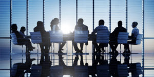 Image of a group of business people sitting around a large table, illustrating the concept of taking minutes of the first board meeting of directors.