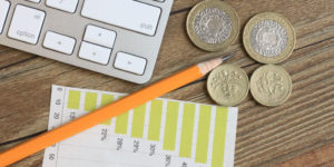 Coins, a pencil, laptop and financial chart sitting on a desktop representing the process of preparing annual accounts.