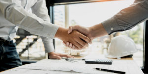 Two business people shaking hands over a desk with documents pens and calculator.