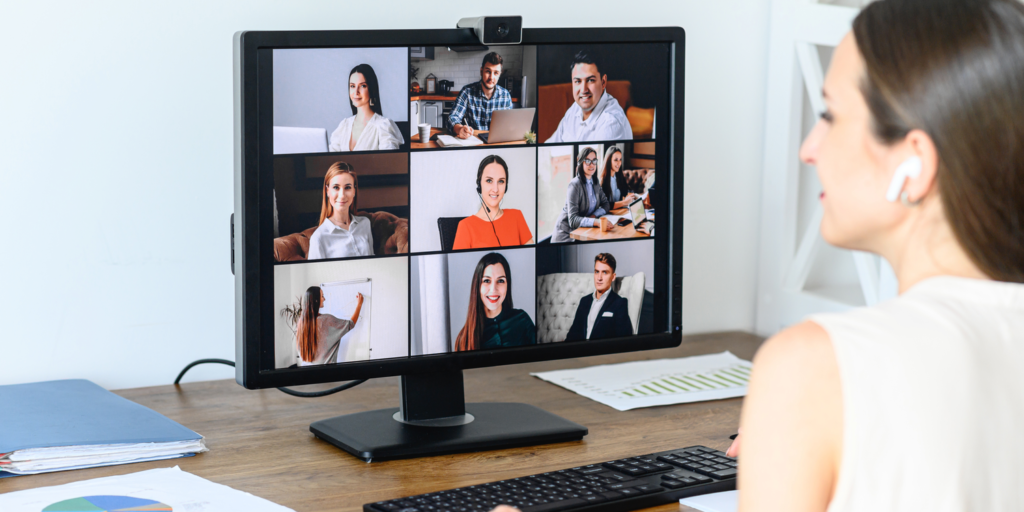 Female business person sitting at desk attending a board meeting using virtual meeting software with other board members visible on monitor.