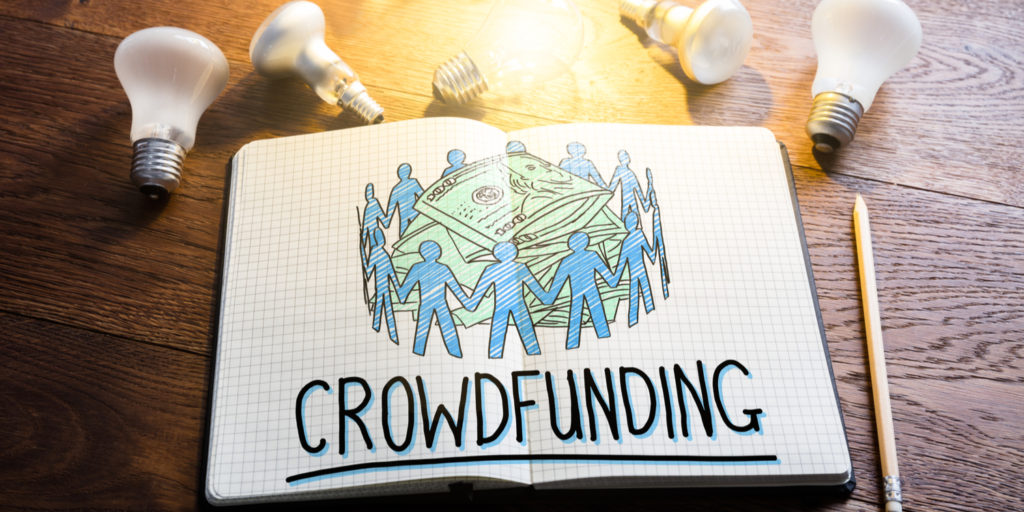 Book lying open with the an image depicting the crowdfunding concept and title 'CROWDFUNDING' with light bulbs lying beside the book.