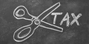 Scissors and the word TAX drawn on a blackboard in white chalk.