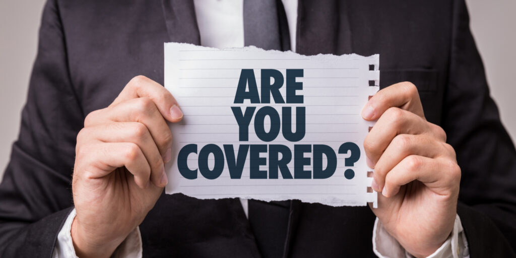 Business person in dark suit holding paper sign displaying 'ARE YOU COVERED?'