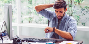 Business person sitting at desk looking at his watch with anxious look.