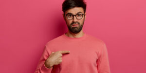 Man in peach jumper pointing to himself