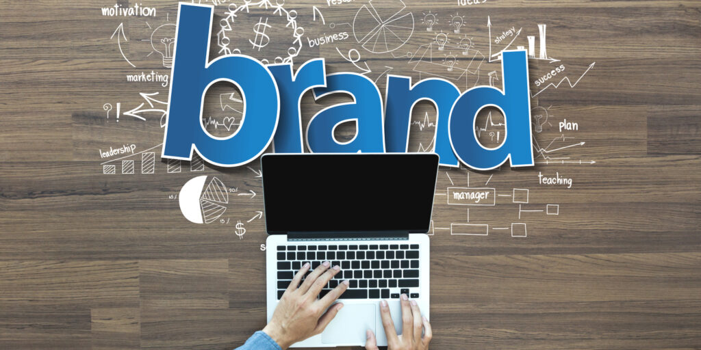 Creative thinking illustration with the word 'brand' highlighted on wooden table background, and businessman working on laptop.