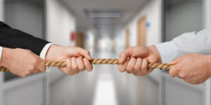 Man in suit and man in shirt playing tug of war in a corridor