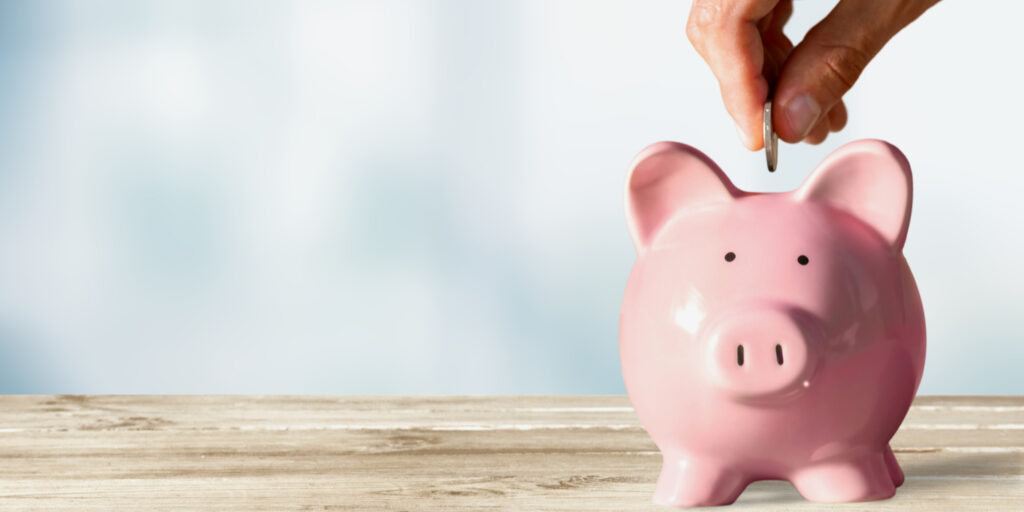 Pink piggy bank on wooden table with hand placing coin in it