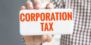 Man's hand showing white card with CORPORATION TAX printed in orange font.