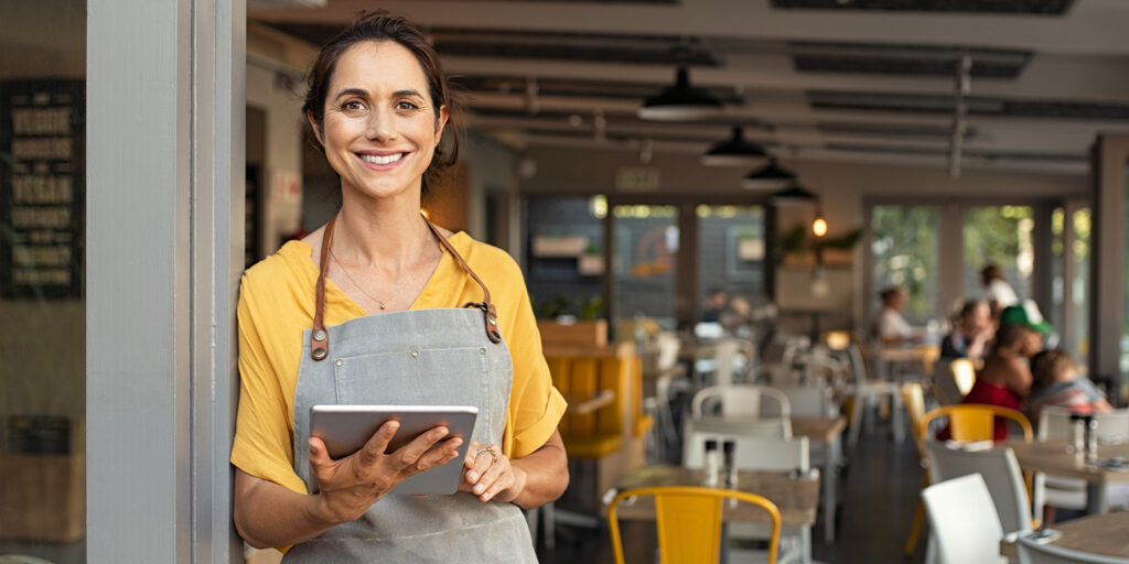 Female business owner standing at front of restaurant holding a tablet