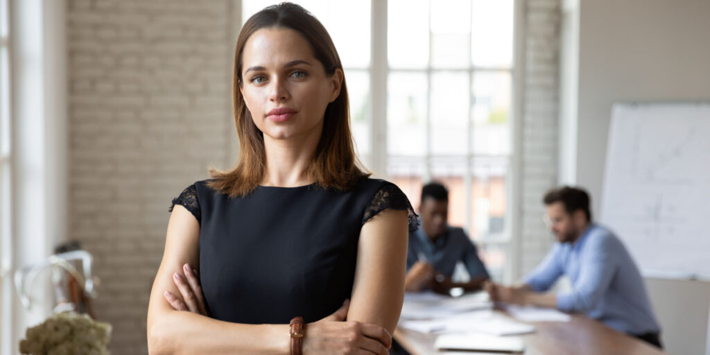 Headshot portrait of focused young sole director standing forefront posing at office meeting.