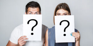 Man and woman hiding their faces behind white cards with question marks, illustrating the concept of anonymity.