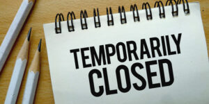 Temporarily Closed text written on a notebook with pencils.