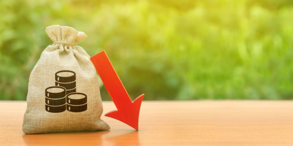 Money bag sitting on a table with a red arrow pointing downward, illustrating concept of reduction of capital.