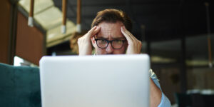 Small business owner working on laptop and holding his temples battling depression and stress.