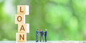 The word LOAN displayed on 4 wooden blocks, with miniature businessmen discussing how to borrow money from their limited company.