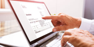 Close-up of a businessperson's hand while creating an invoice on a laptop at the workplace.