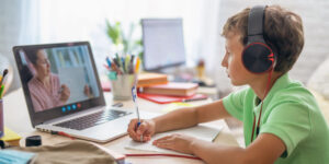 Small boy with headphones on a video call with his online tutor using his laptop.