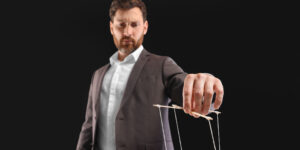 A shadow director in a brown suit with white shirt pulling the strings of a puppet, demonstrating the control a shadow director has over a company.