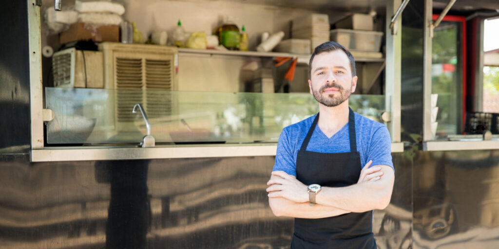 Portrait of a food-to-go business owner proudly standing in front of his food truck.