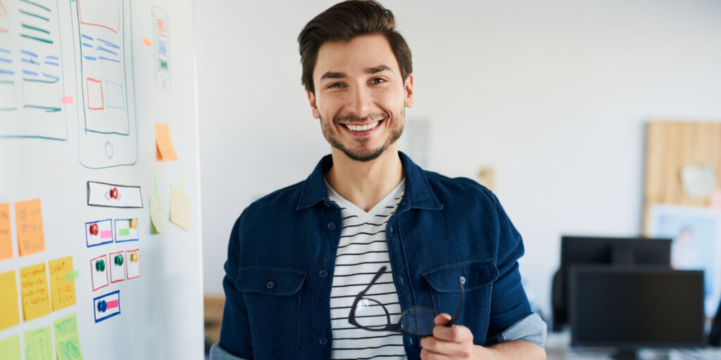 Happy freelance web developer standing in office beside a white board.