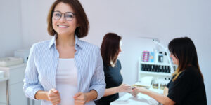 Female nail salon owner looking at the camera and smiling with nail salon in background.