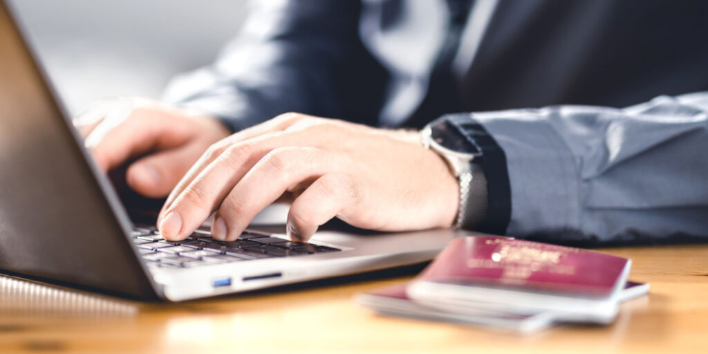 Man working at a laptop with 2 passports sitting on the desk.