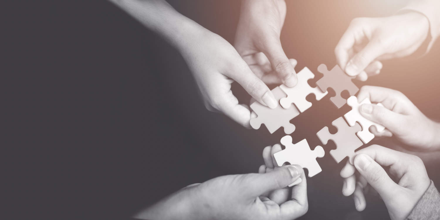 Hands bringing jigsaw pieces together, representing the concept of separate companies coming together to create a holding company.
