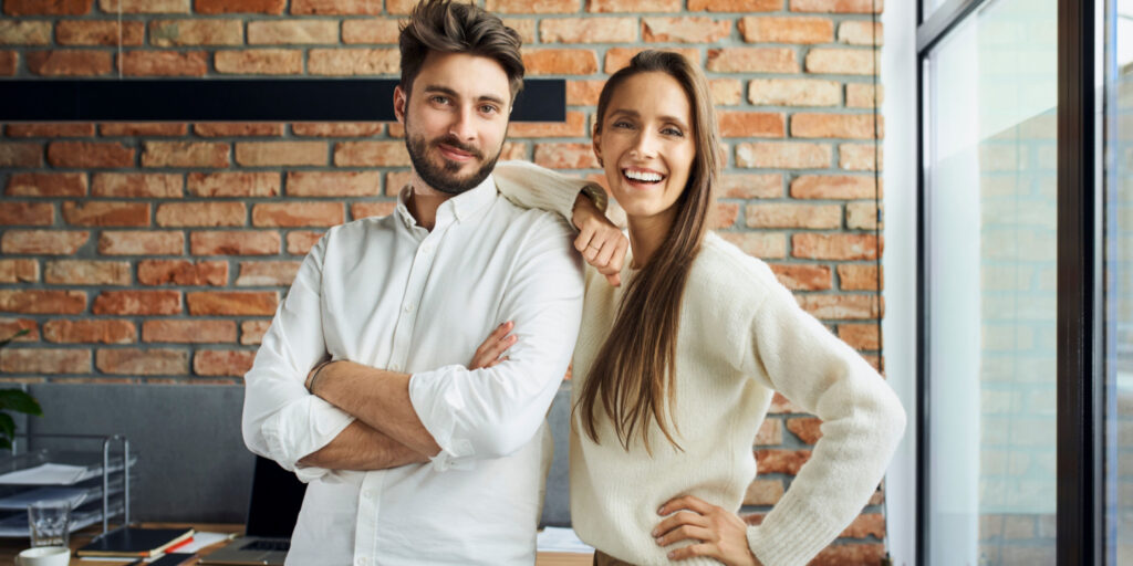 Portrait of successful couple standing at small office. Happy new business partners posing together.