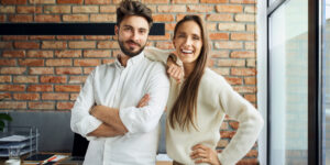 Portrait of successful couple standing at small office. Happy new business partners posing together.