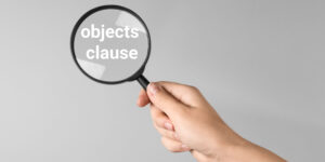 A female hand holding a magnifying glass with the words 'objects clause' within the glass, on a grey background.