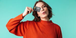 Pretty young female business owner dressed in sweater holding bank card to her face with a green background.