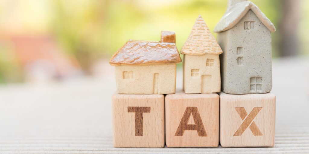 The word TAX is displayed on 3 wooden blocks with miniature homes sitting on top of the blocks.