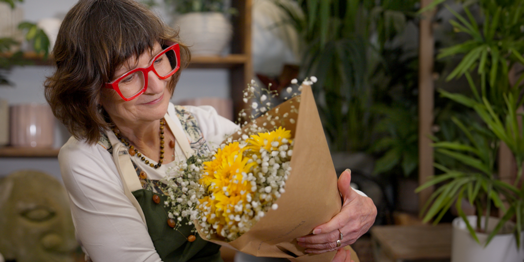 Mature female business owner with large red rimmed spectacles holding a bunch of flowers in her florist shop.