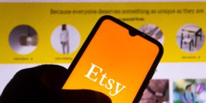 A hand holding a smartphone with the ETSY logo displayed on the screen.