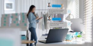 Chatbot conversation on laptop screen app interface with artificial intelligence technology providing virtual assistant customer support, with female business owner in background.