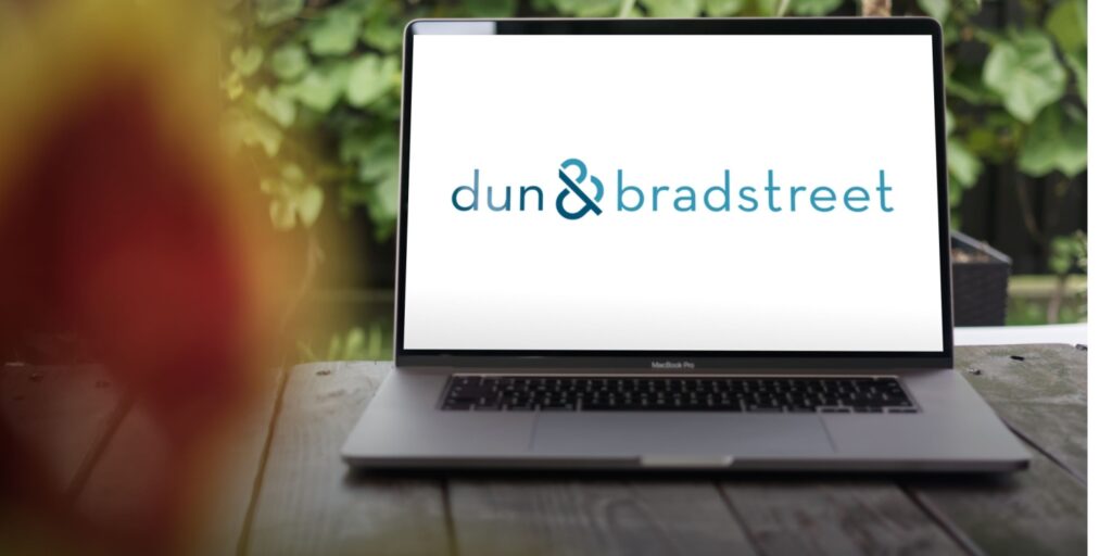 The Dun & Bradstreet logo displayed on the screen of a MacBook Pro sitting on a wooden table.