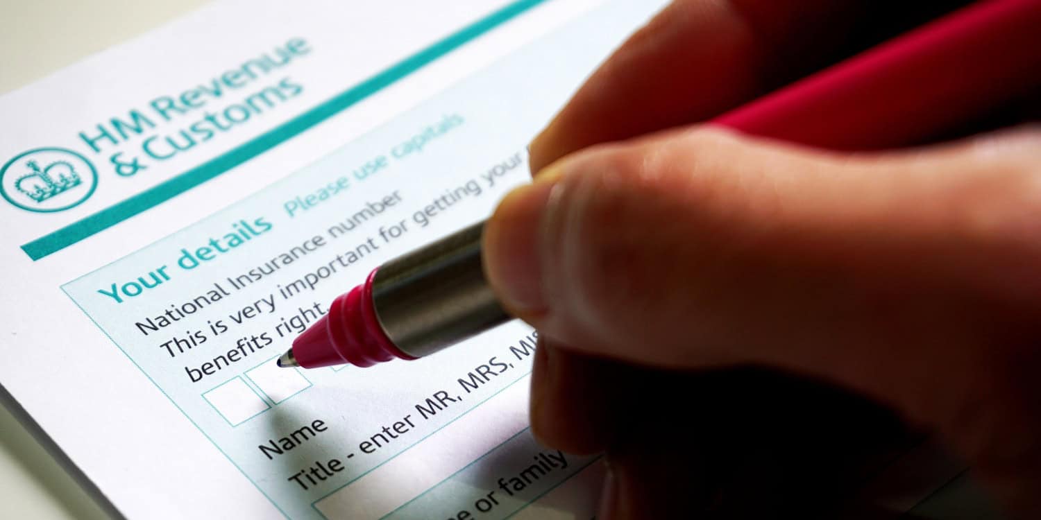 Photo of a hand holding a pen and filling in a Self Assessment tax return form for HMRC