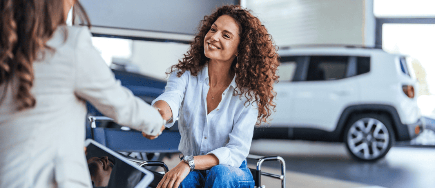 Satisfied customer at a car dealership buying a new car. She's smiling and shaking the sales representative's hand.