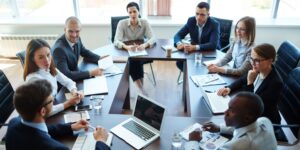 Meeting of eight company shareholders in a modern conference room, wearing business suits.