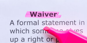 The word 'waiver' printed on white paper and highlighted with pink highlighter pen, with a partial definition shown underneath.