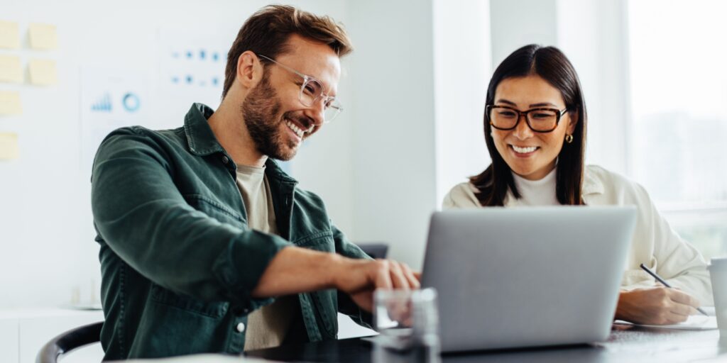 Two people working from a laptop. One is smiling and pointing at the screen.