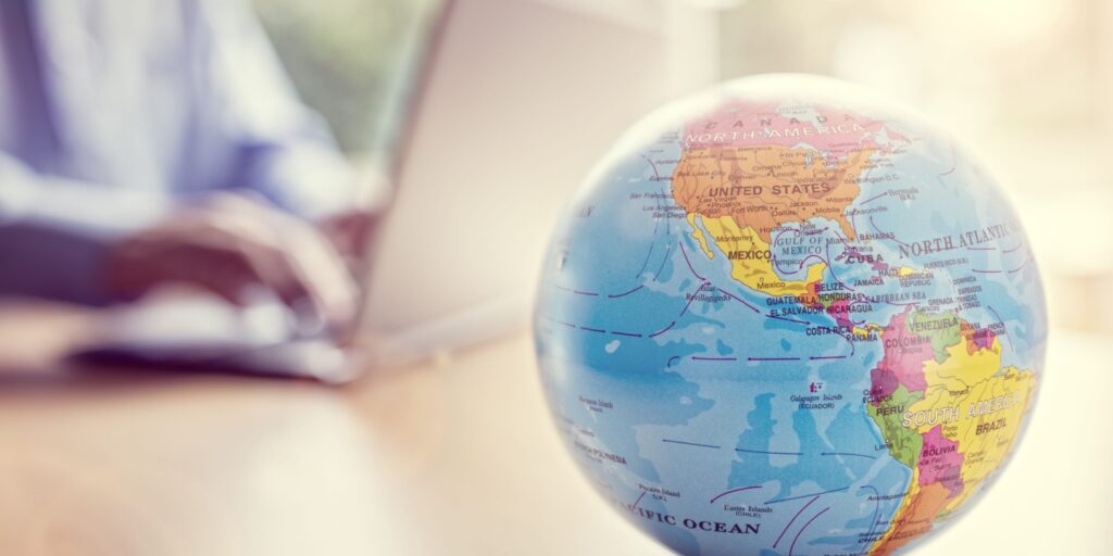 Image of a globe placed on a desk with a person sat typing on a laptop behind it.