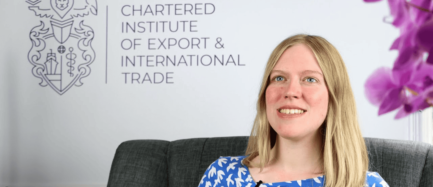 Grace Thompson, UK Public Affairs Lead at the Chartered Institute of Export & International Trade, sits for an interview in a close-up shot, with the institute’s branding on a blank wall behind her