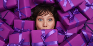 Portrait of female with a surprised look, surrounded by purple gift boxes with blue ribbons tied in a bow.