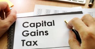 A person's hands holding a document with Capital Gains Tax printed on the front.