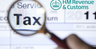 Magnifying glass held over an HMRC tax return form, highlighting the word 'Tax'.